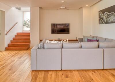 Spacious and well-lit living room with a modern configuration and staircase, decorated with art.