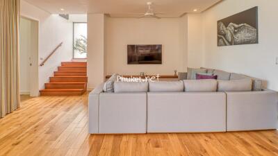 Spacious and well-lit living room with a modern configuration and staircase, decorated with art.