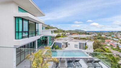 Modern multi-story building with balconies, glass windows, and a pool, overlooking a scenic view