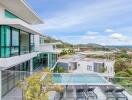 Modern multi-story building with balconies, glass windows, and a pool, overlooking a scenic view