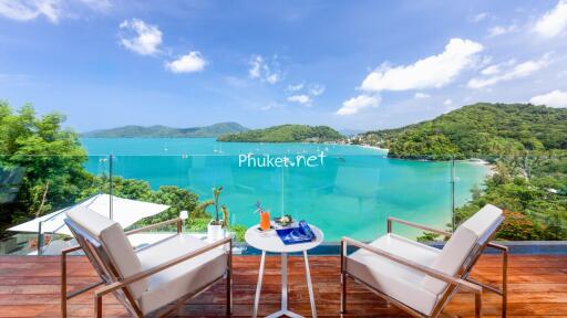 Stunning balcony view of the ocean and surrounding hills with cozy seating.