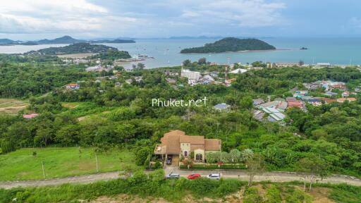 Aerial view of a large house with a red roof and surrounding green landscape, overlooking the sea and islands in the distance.