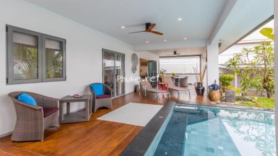 Covered patio with seating area, ceiling fans, and an adjacent pool in a tropical garden setting