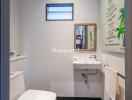 Small bathroom with toilet, sink, mirror, and wall art