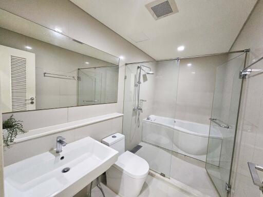 Modern bathroom with glass shower, bathtub, sink, and toilet