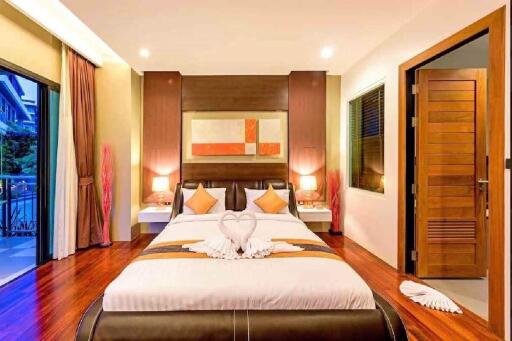 Modern bedroom with wooden flooring, a large bed, balcony, and ambient lighting