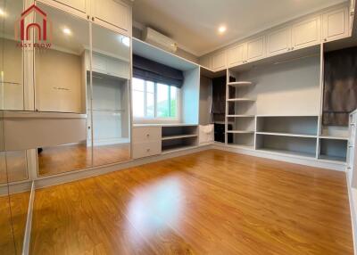 Spacious bedroom with wooden flooring, large built-in wardrobe, shelves and a window with natural lighting