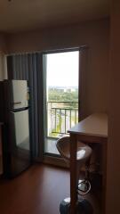 A compact kitchen area with a refrigerator, countertop, and a chair next to a balcony offering scenic views.