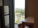 A compact kitchen area with a refrigerator, countertop, and a chair next to a balcony offering scenic views.