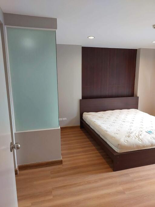 Modern bedroom with wooden floor, a large bed, and a glass partition