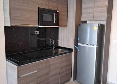 Modern kitchen with wooden cabinets, black countertops, microwave, and stainless steel refrigerator