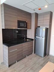 Modern kitchen with wooden cabinets, black countertops, microwave, and stainless steel refrigerator