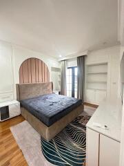 Modern bedroom with built-in shelves, a large bed, hardwood flooring, and balcony access