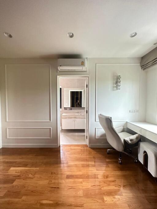 Home office with wooden floors, desk, office chair, and view into an adjacent bathroom