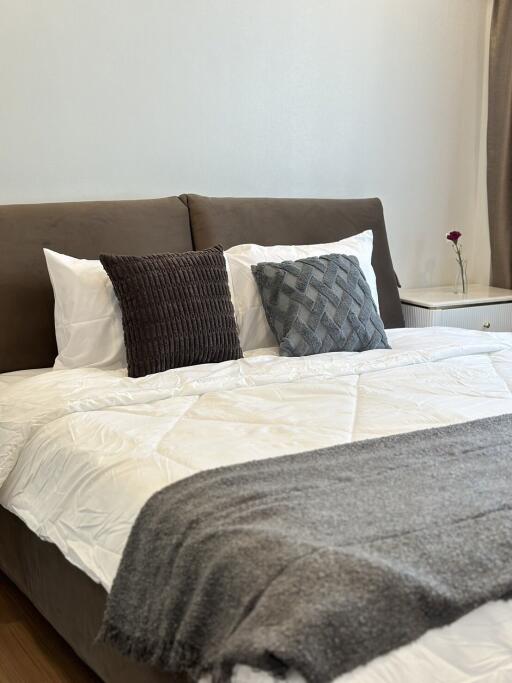 Cozy bedroom with a neatly made bed, decorative pillows, a bedside table, and a flower vase