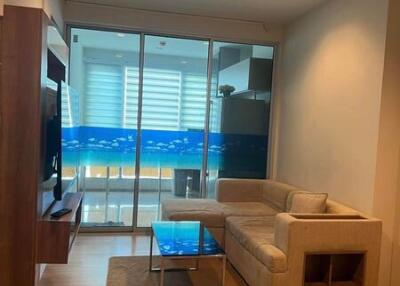 Living room with a beige corner sofa, glass coffee table, wooden flooring, and a sliding glass door leading to a balcony