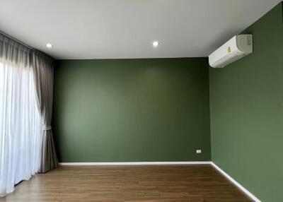 Empty living room with green walls, wooden flooring, ceiling lights, and an air conditioner