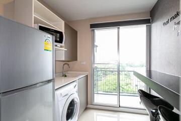 Modern kitchen with a washing machine, refrigerator, microwave, sink, countertop, and large window with a balcony view.