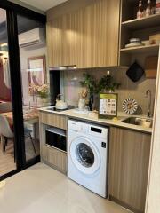 Small modern kitchen with washing machine, sink, microwave, and upper cabinets.