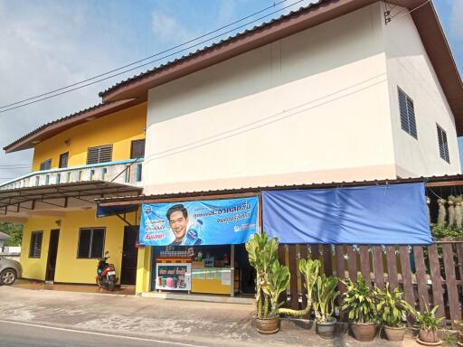 Two-story building with a yellow and white exterior, balcony, and blue awning