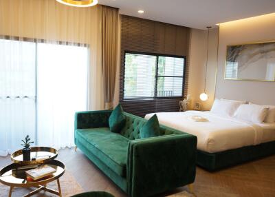 Modern bedroom with a bed, green velvet sofa, and large windows