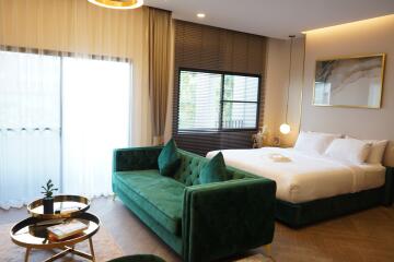 Modern bedroom with a bed, green velvet sofa, and large windows