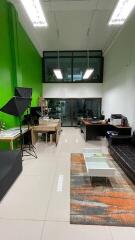 Modern living area with high ceiling, green accent wall, glass window, and office setup