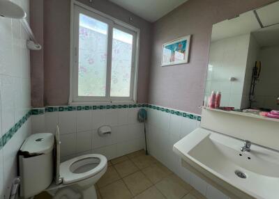 Bathroom with tiled walls and floor, featuring a toilet, sink, mirror, and window.