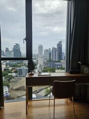 View of cityscape from bedroom with large window, desk, and chair