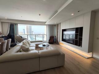 Modern living room with large windows, sectional sofa, wall-mounted TV, and city view