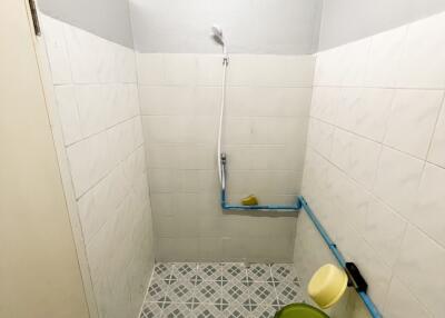 Bathroom with tiled walls and floor, a showerhead, a green bucket, and blue pipes