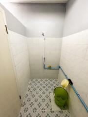 Bathroom with tiled walls and floor, a showerhead, a green bucket, and blue pipes