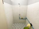 Bathroom with tiled walls and floor, a showerhead, a green bucket, and blue pipes