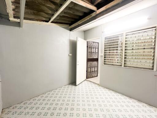 An empty room with tiled flooring, a door, and a window with metal bars.