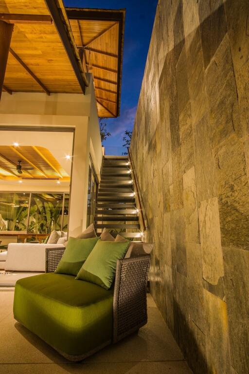 Outdoor seating area with large stone wall, green cushioned seating, and steps leading to upper level