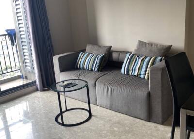 Living room with gray sofa, two striped pillows, round glass coffee table, and access to balcony