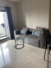 Living room with gray sofa, two striped pillows, round glass coffee table, and access to balcony