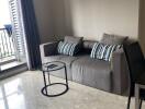 Living room with gray sofa, two striped pillows, round glass coffee table, and access to balcony