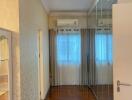 A polished wooden floor hallway with large mirrored wardrobes and a window with modern curtains