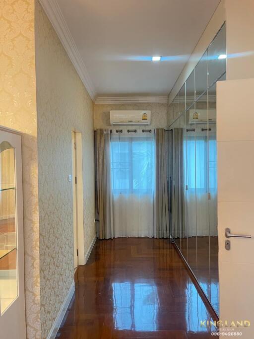 A polished wooden floor hallway with large mirrored wardrobes and a window with modern curtains