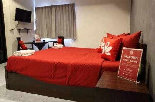 Bedroom with a double bed featuring red pillows and bedsheet, a wall-mounted TV, and a small seating area with a table and two chairs.