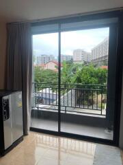 Living room with sliding glass door leading to a balcony with a view of other buildings and greenery