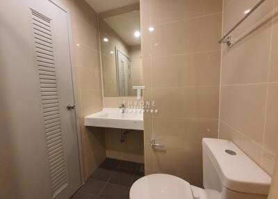 Bathroom with a toilet, sink, mirror, and tiled walls