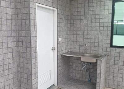 Small basic kitchen area with tiled walls, sink, and white door