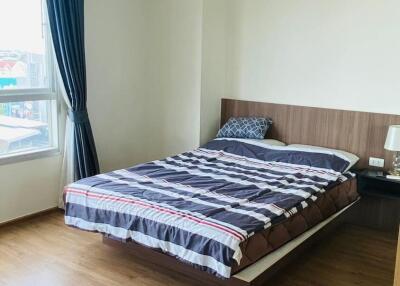 Bedroom with wooden floor, bed, nightstand, and large window with blue curtains