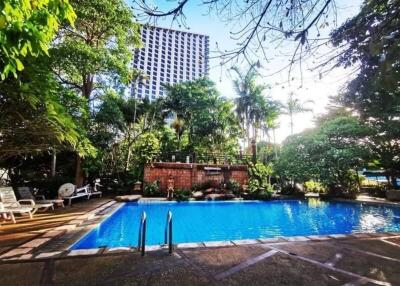 Outdoor swimming pool with lush greenery and tall buildings in background