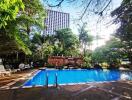 Outdoor swimming pool with lush greenery and tall buildings in background