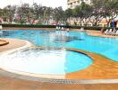 Outdoor swimming pool with people, lounge chairs, trees, and buildings in the background