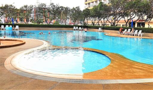 Outdoor swimming pool with people, lounge chairs, trees, and buildings in the background