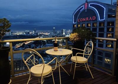 Night-time cityscape view from a balcony with a small table and two chairs